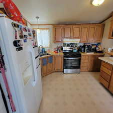 Kitchen featuring light flooring, light countertops, white refrigerator with ice dispenser, stainless steel gas stove, and wood finish cabinets