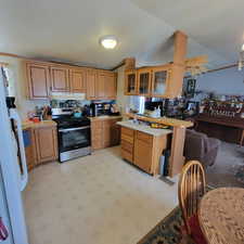 Kitchen with light countertops, glass fronted cabinets, wood finish cabinets, stainless steel range with gas stovetop, and vaulted ceiling