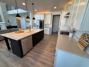 Kitchen featuring open floor plan, stainless steel appliances, a center island with sink, light wood-type flooring, and light stone counters