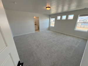 Unfurnished bedroom with light carpet, connected bathroom, and a textured ceiling