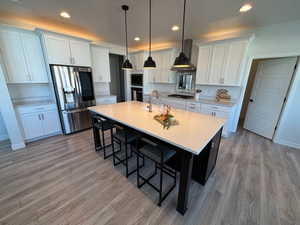 Kitchen with stainless steel appliances, a center island with sink, a breakfast bar, two tone color scheme, and light wood-type flooring