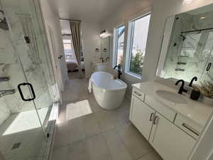 Bathroom with a marble finish shower, connected bathroom, two vanities, and healthy amount of natural light