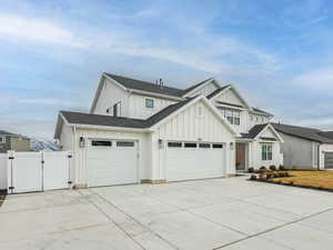 Modern farmhouse featuring a gate, board and batten siding, concrete driveway, a shingled roof, and an attached garage