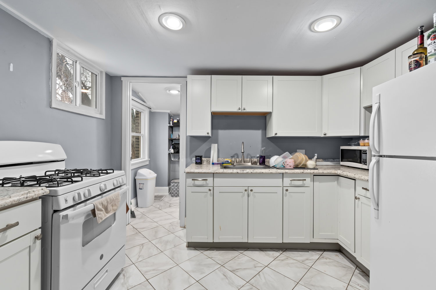 Kitchen featuring white appliances, white cabinetry, light marble finish flooring, and light stone countertops