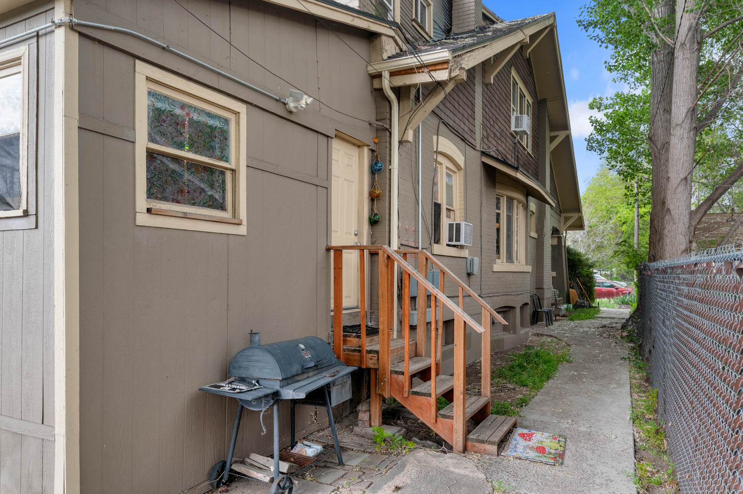 Exterior siding with multiple windows, featuring a wooden staircase and a concrete walkway