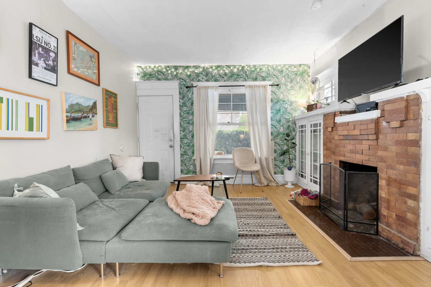 Living area with wallpapered walls, light wood-type flooring, a brick fireplace, and an accent wall