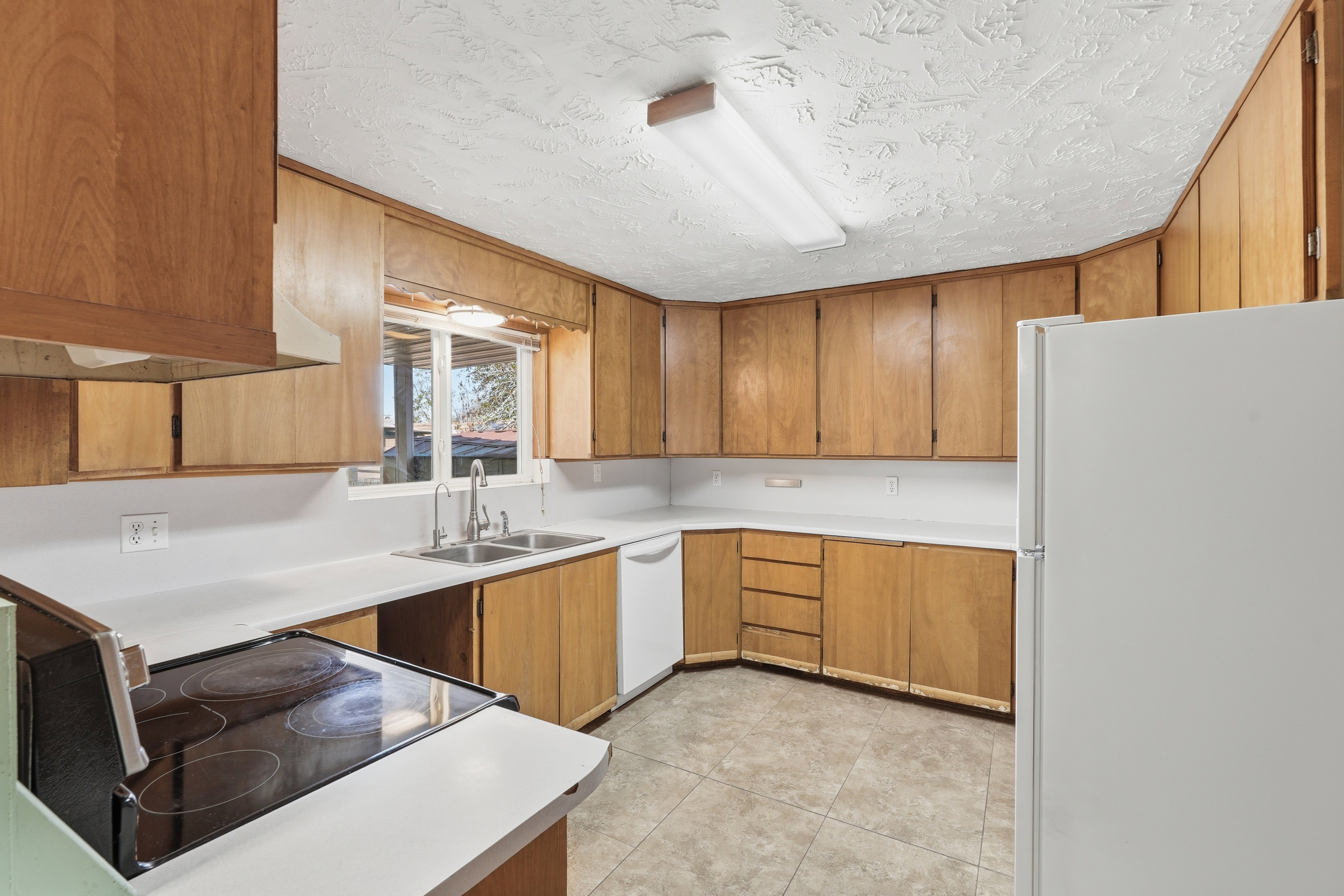 Kitchen featuring white appliances, light countertops, wood finish cabinets, a textured ceiling, and light tile patterned floors