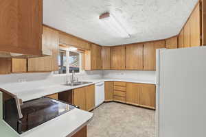 Kitchen featuring white appliances, light countertops, wood finish cabinets, a textured ceiling, and light tile patterned floors