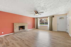 Unfurnished living room with light wood-type flooring, a textured ceiling, ceiling fan, and a fireplace