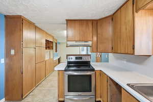 Kitchen featuring electric range, light countertops, a textured ceiling, wood finish cabinetry, and light tile patterned flooring