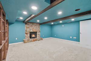 Unfurnished living room with carpet, beamed ceiling, a stone fireplace, a textured ceiling, and recessed lighting
