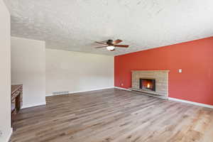 Unfurnished living room with light wood-style floors, a fireplace, a ceiling fan, and a textured ceiling
