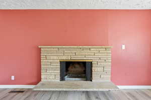 Detailed view of a textured ceiling, a stone fireplace, and wood finished floors