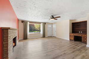 Unfurnished living room with built in study area, a ceiling fan, light wood-type flooring, a lit fireplace, and a textured ceiling