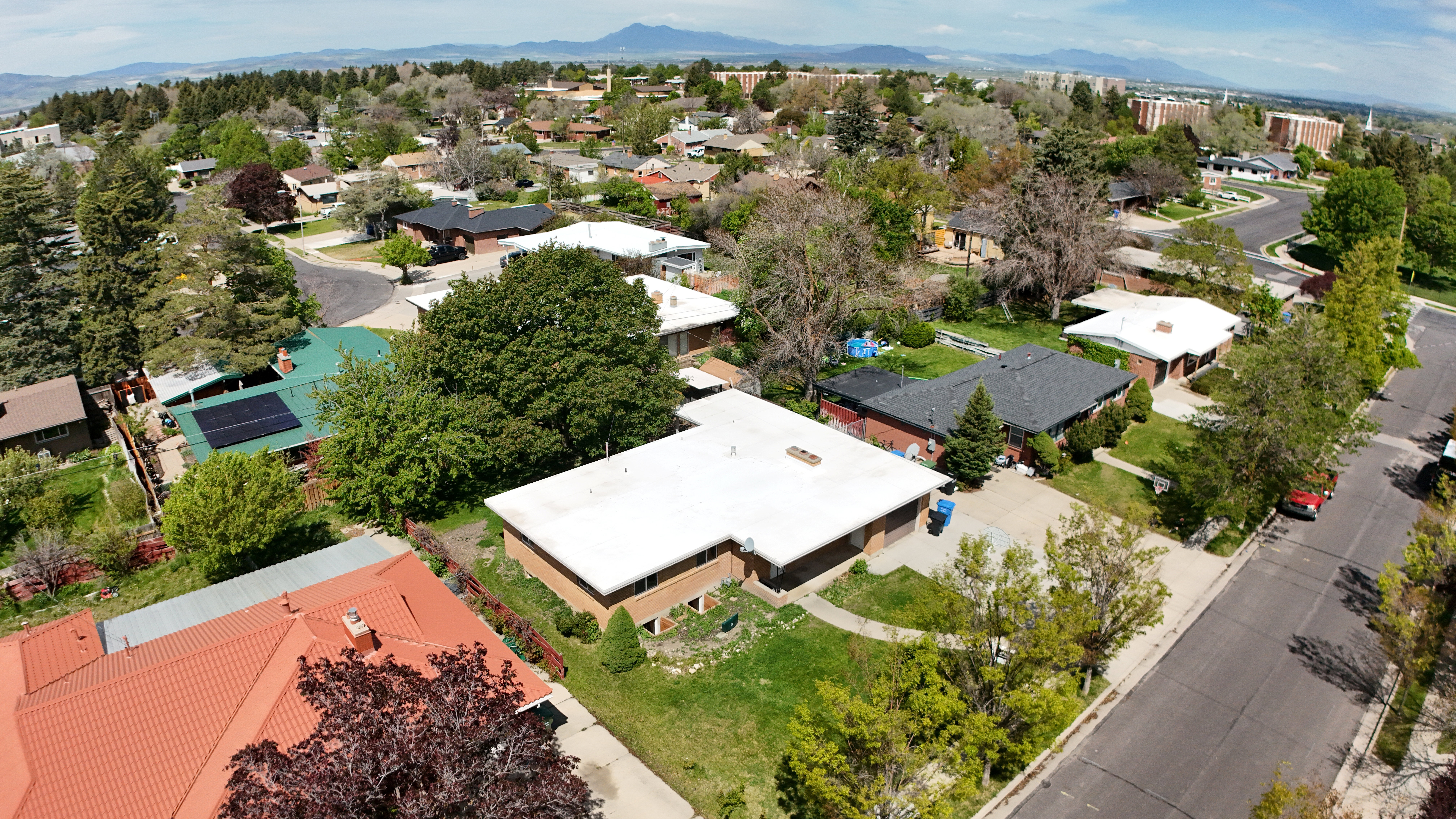 Suburban street featuring various residential properties, mature trees, and mountainous terrain in the distance