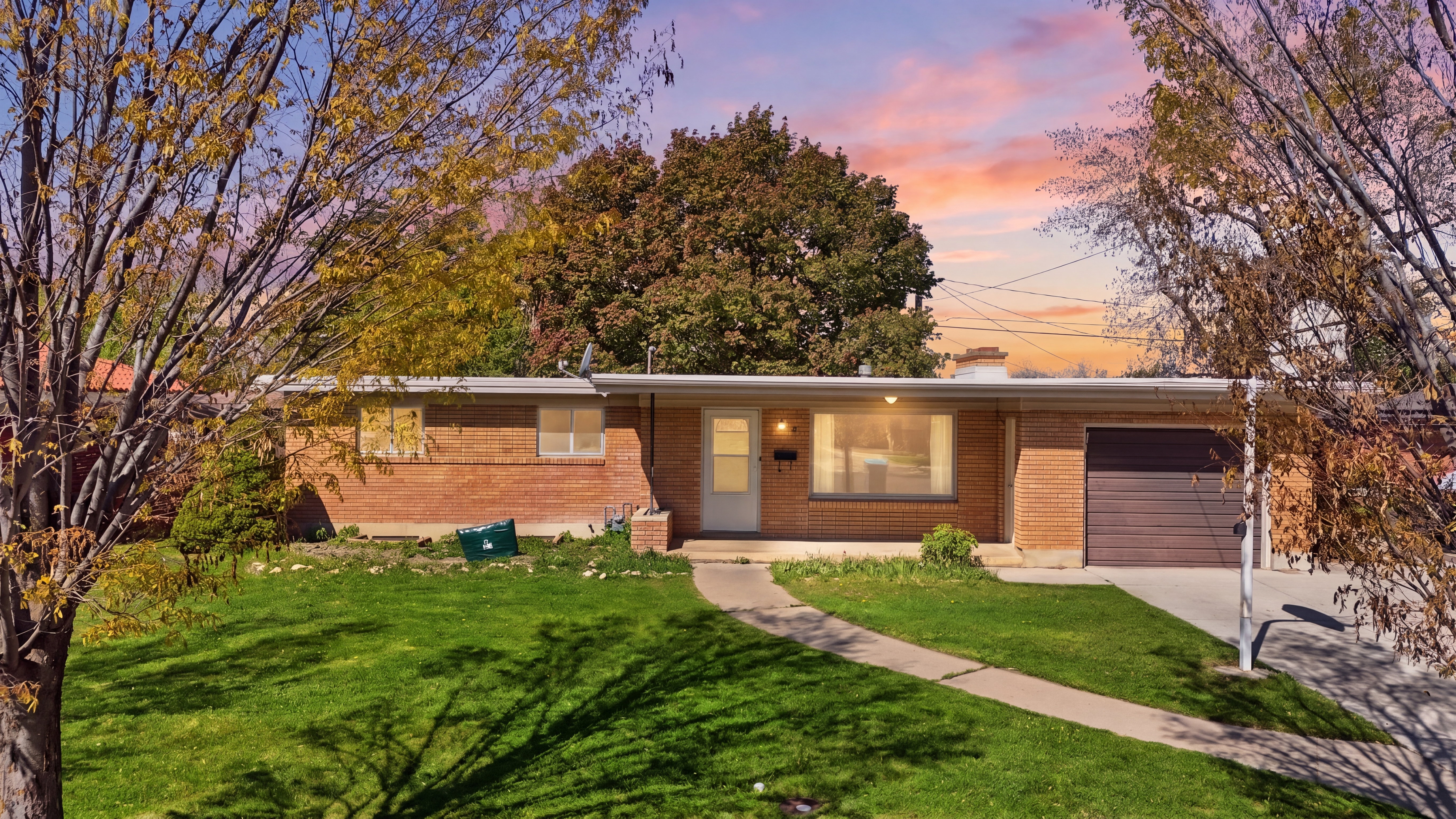 Ranch-style home featuring an attached garage, a yard, brick siding, concrete driveway, and a chimney