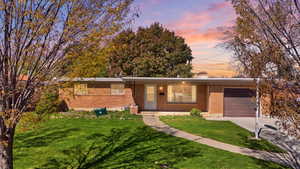 Ranch-style home featuring an attached garage, a yard, brick siding, concrete driveway, and a chimney