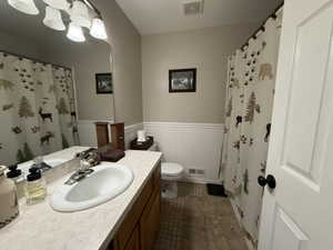 Bathroom featuring wainscoting, vanity, a shower with shower curtain, and dark tile patterned flooring