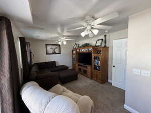 Carpeted living room with a ceiling fan and baseboards