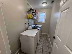 Laundry room with a textured ceiling, washing machine and clothes dryer, and light tile patterned floors
