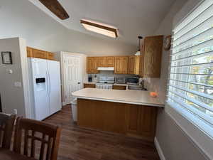 Kitchen with a peninsula, light countertops, white appliances, hanging light fixtures, and wood finish cabinetry