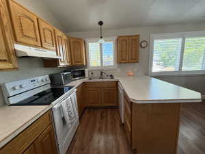Kitchen featuring white electric stove, a peninsula, light countertops, decorative light fixtures, and lofted ceiling