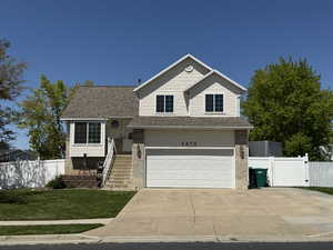 Tri-level home featuring a shingled roof, concrete driveway, a garage, and a gate