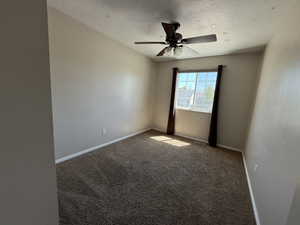 Spare room with dark colored carpet, a ceiling fan, and a textured ceiling