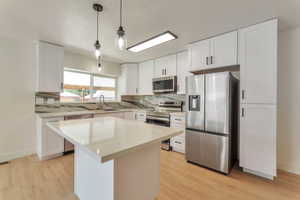 Kitchen with stainless steel appliances, white cabinets, light stone counters, hanging light fixtures, and backsplash