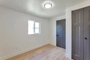 Unfurnished bedroom featuring a textured ceiling, light wood finished floors, and a closet