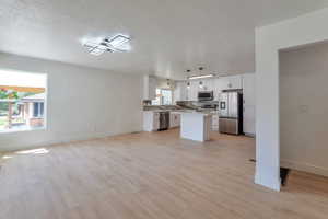 Kitchen with open floor plan, white cabinets, a center island, light countertops, and stainless steel appliances