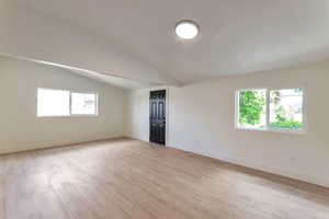 Unfurnished room with light wood-style flooring and vaulted ceiling