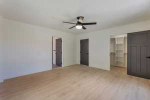 Unfurnished bedroom with a walk in closet, light wood-style flooring, and a ceiling fan