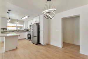 Kitchen featuring suspended lighting, stainless steel appliances, white cabinetry, and light wood finished floors