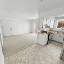 Kitchen with light colored carpet, stainless steel appliances, light countertops, white cabinets, and open floor plan