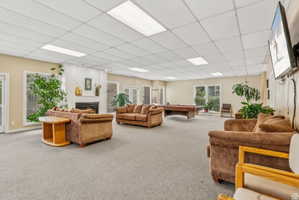 Living room featuring carpet flooring, a drop ceiling, a lit fireplace, and billiards