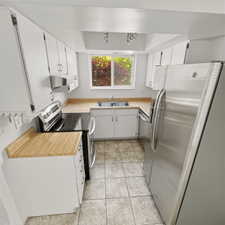 Kitchen with light countertops, stainless steel appliances, white cabinets, and light tile patterned floors