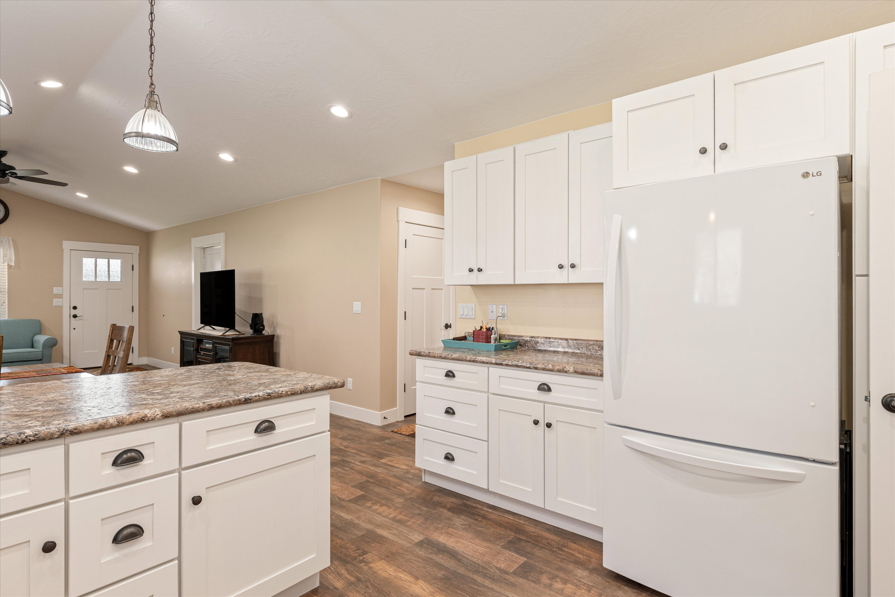 Kitchen with freestanding refrigerator, white cabinets, lofted ceiling, dark wood-style flooring, and pendant lighting
