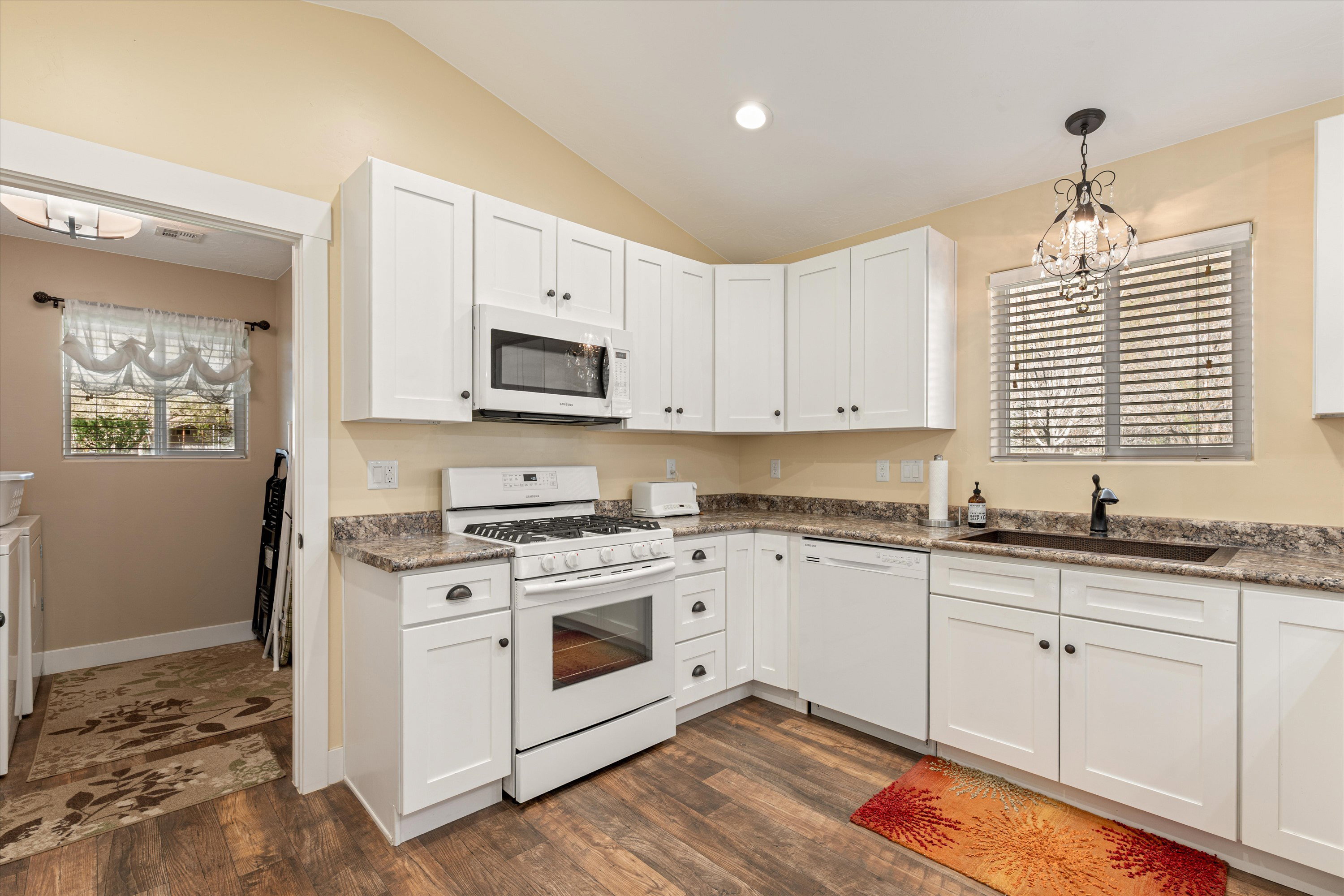 Kitchen featuring white appliances, white cabinets, lofted ceiling, hanging lights, and dark wood-type flooring