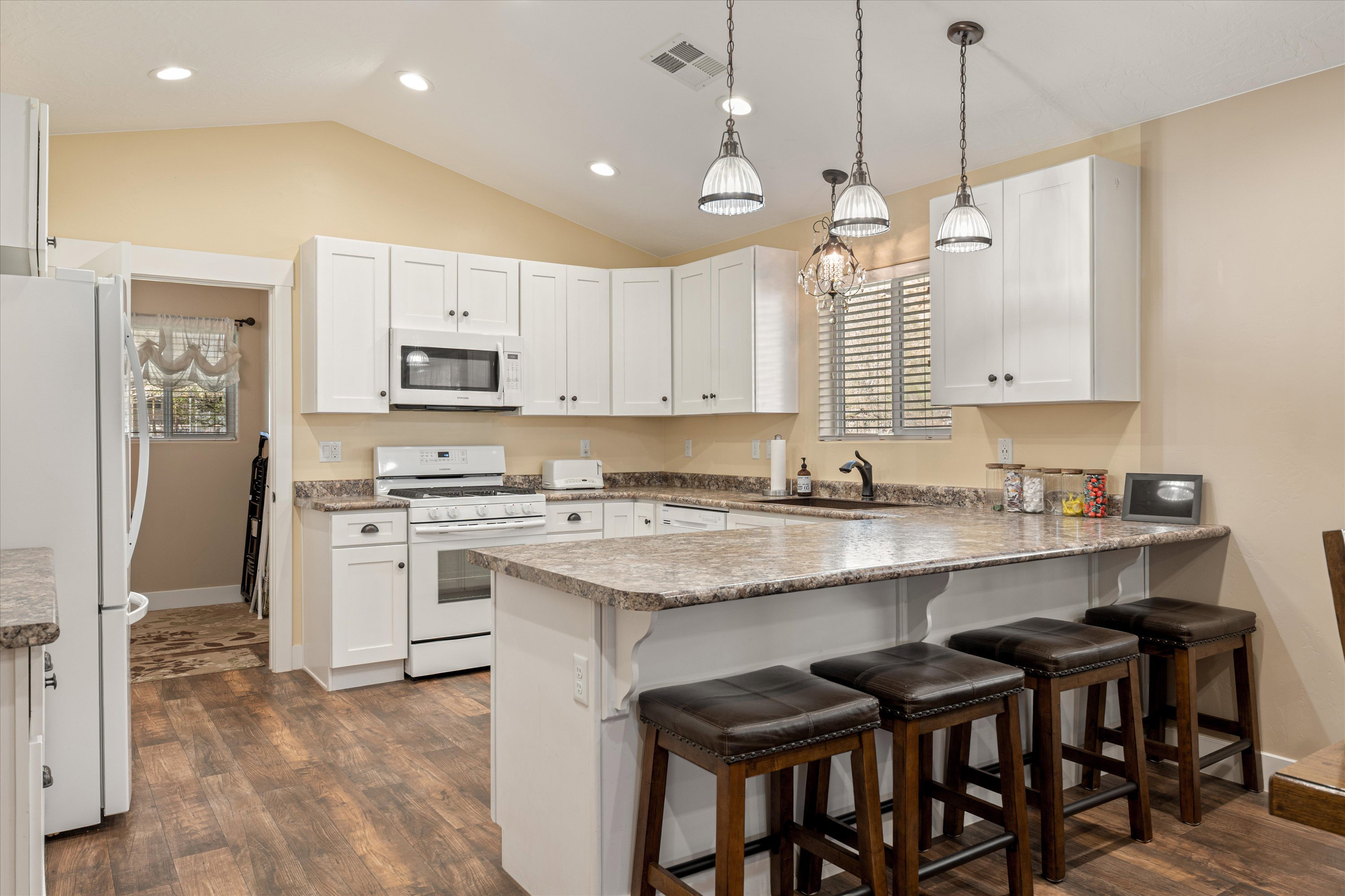 Kitchen with a kitchen bar, white appliances, a peninsula, decorative light fixtures, and white cabinetry