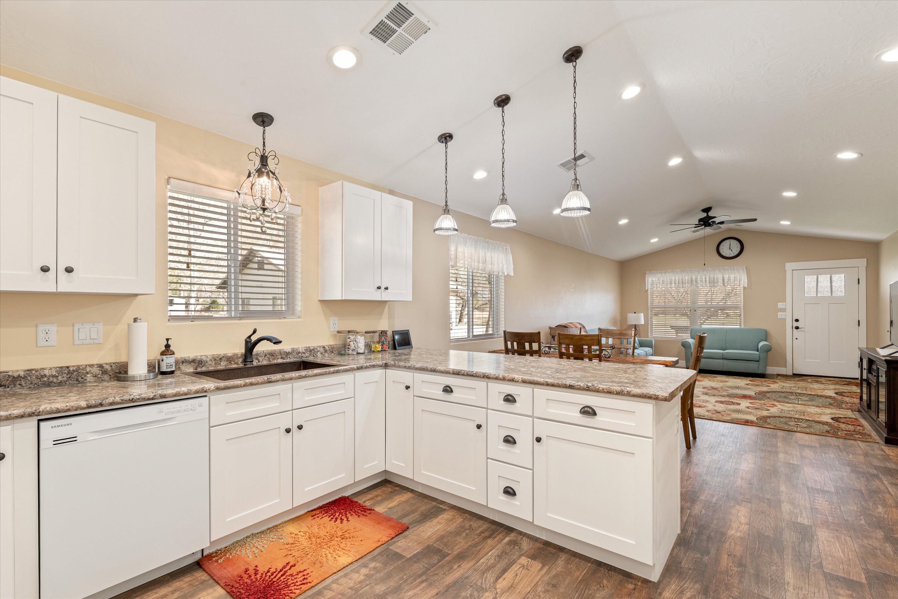 Kitchen with a peninsula, white cabinets, dishwasher, open floor plan, and dark wood-style flooring
