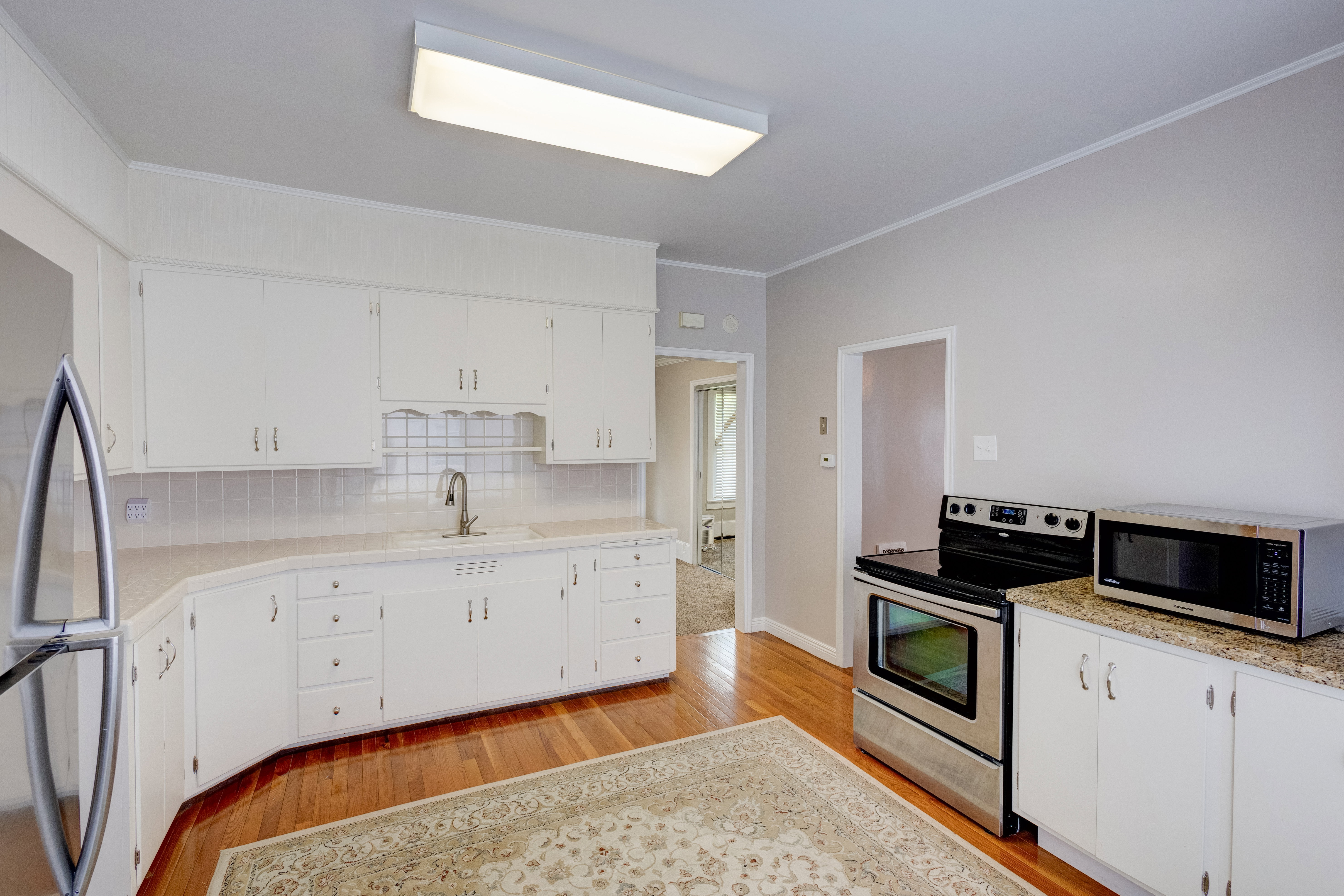 Kitchen featuring ornamental molding, stainless steel appliances, light countertops, white cabinetry.