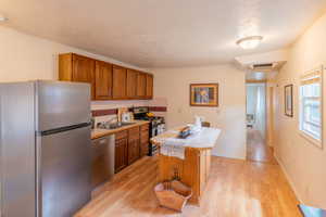 Kitchen featuring stainless steel appliances, light countertops, wood finish cabinets, light wood finished floors, and a kitchen island