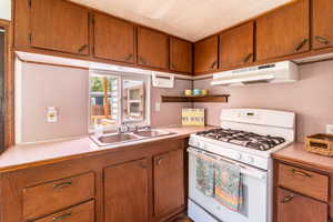 Kitchen featuring white range with gas stovetop, wood finish cabinetry, light countertops, and a textured ceiling