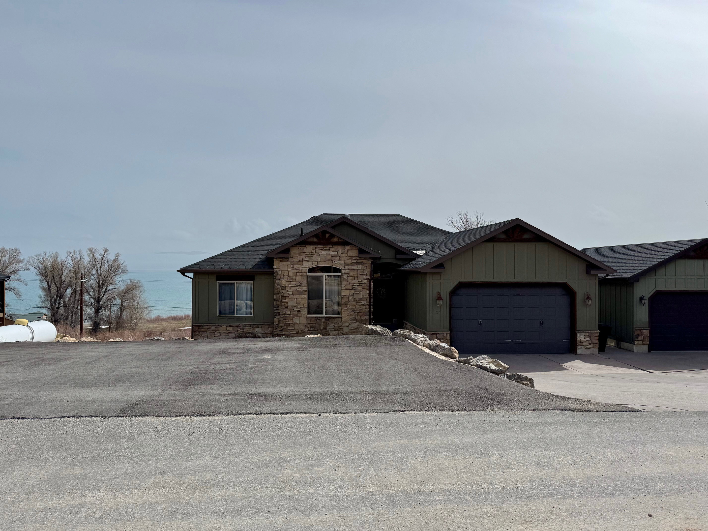 Large parking area at front of house featuring stone siding, two 2-car garage, plus detached garage, driveway, and roof with shingles