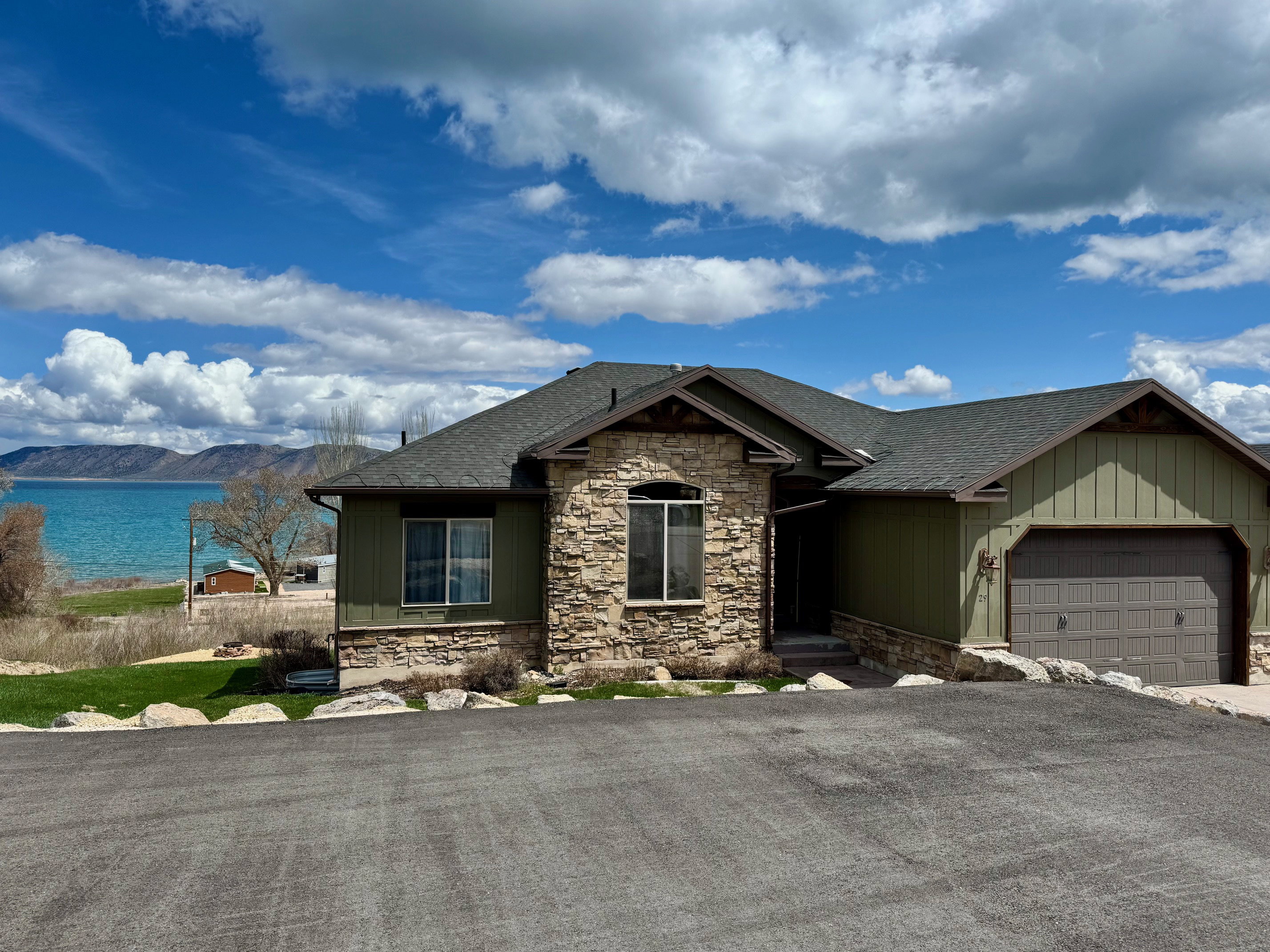 View of front of property featuring stone siding, an attached garage, a shingled roof, and a lake mountain view