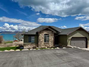 View of front of property featuring stone siding, an attached garage, a shingled roof, and a lake mountain view
