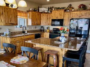 Kitchen with dark stone countertops, wood finish cabinets, black appliances, a kitchen island, and a kitchen bar