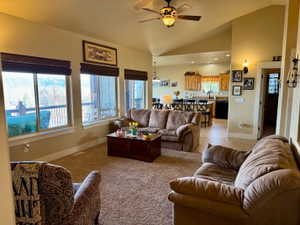 Living room featuring a ceiling fan, vaulted ceiling, large windows with lake view