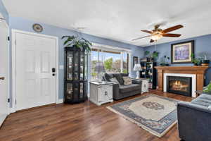 Living room featuring dark wood-type flooring, a ceiling fan, a glass covered fireplace, and a textured ceiling